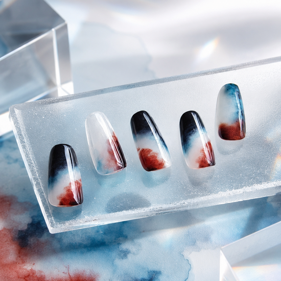 A set of five decorative press-on nails displayed in a clear acrylic tray, featuring a glossy black and white gradient design with red and blue marbled accents, set against a stylized background with watercolor splashes and geometric acrylic blocks.